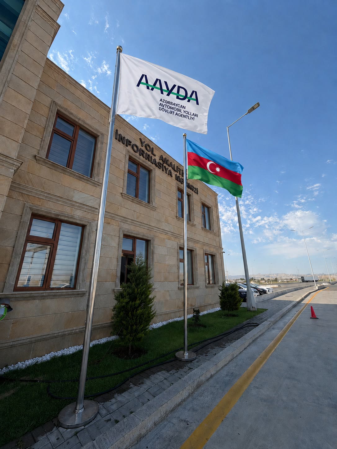 AAYDA Yol Analitika ve İnformasiya Merkezi binasının önünde NERJ METAL üretimi iki paslanmaz çelik bayrak direği: birinde AAYDA bayrağı, diğerinde Azerbaycan bayrağı.